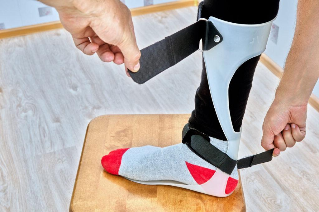 A person putting a brace on their leg and foot using orthopedic straps.